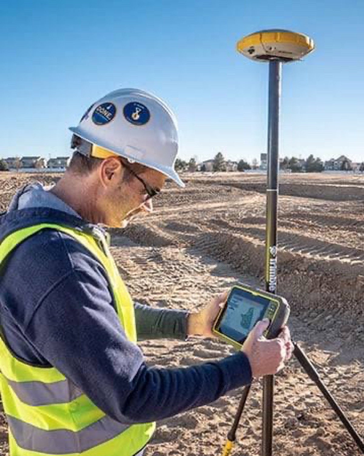 Construction worker using a Trimble GNSS rover and field controller on graded soil
